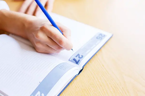 Close up view millennial woman sit at table hold pencil take notes to paper notebook working studying. Female student businesswoman employee write records to daily planner by hand at home work desk