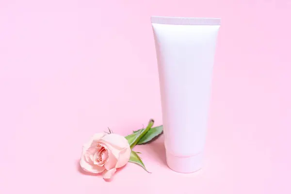White empty cosmetic tube, on a pink background with delicate pink roses. Natural cosmetics with rose extract or skin care spa salon or organic spa salon mockup