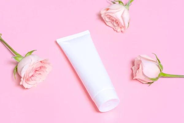 White empty cosmetic tube, on a pink background with delicate pink roses. Natural cosmetics with rose extract or skin care spa salon or organic spa salon mockup