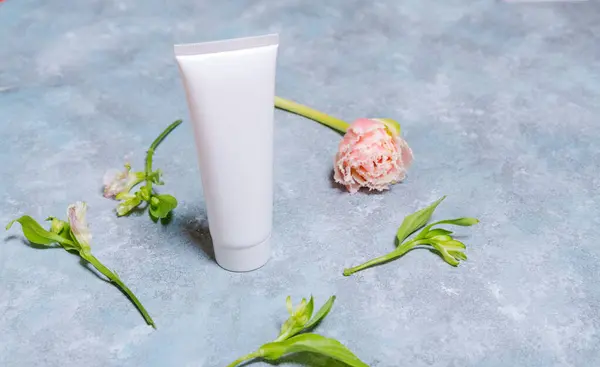 White tube for cream. Branding concept and roses. Tulips on a blue background. Cosmetic skin care product empty plastic bag. White unbranded lotion, balm, hand cream, toothpaste mockup.