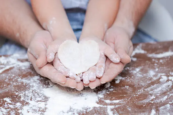 Top view father and childs hand, cut out heart shaped cookies from dough on hands on the background of a wooden table with loose flour. Flat failure.