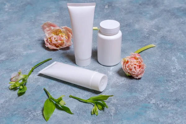 White tube for cream. Branding concept and roses. Tulips on a blue background. Cosmetic skin care product empty plastic bag. White unbranded lotion, balm, hand cream, toothpaste mockup.