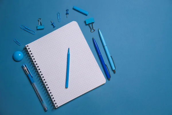 Stationery. Open notebook pencils and pens, stickers and binding clips. Copy space and notes. Writing tools. Office tools. Isolated on blue background