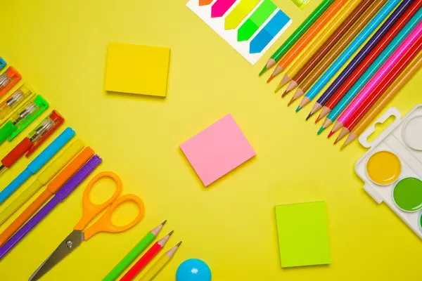 School supplies for drawing, paints colored pencils and pens paper stickers bright stationery on a yellow background, back to school concept