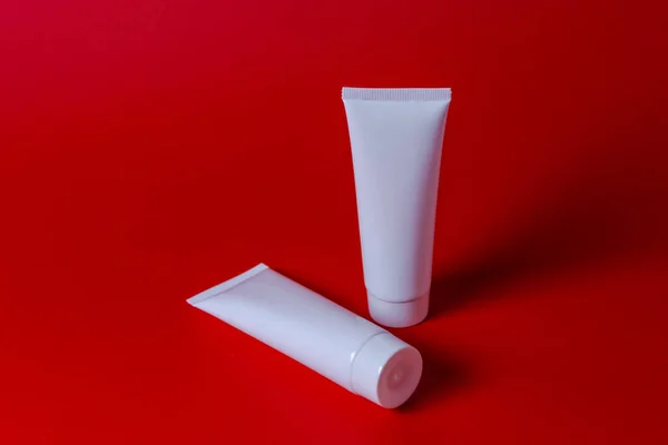 White plastic tube mockup for cosmetic product. Hand cream containers, moisturizer body lotion, face cleanser or shampoo on pastel red background
