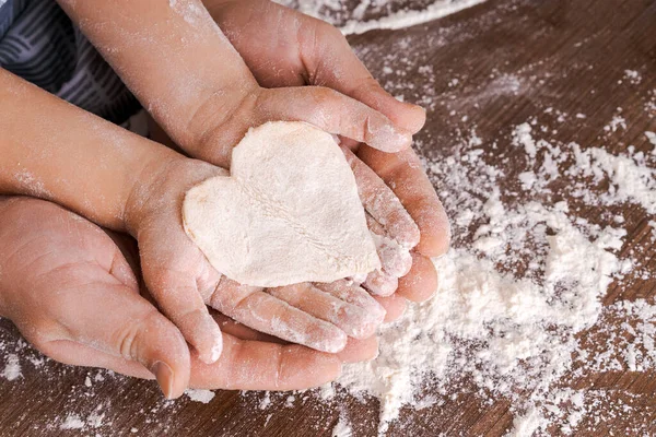 Top view father and childs hand, cut out heart shaped cookies from dough on hands on the background of a wooden table with loose flour. Flat failure.