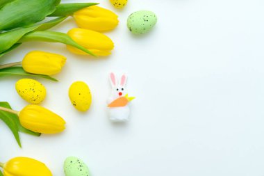 Sarı laleli Paskalya tavşanı oyuncağı ve beyaz arka planda renkli benekli yumurtalar. Paskalya kutlaması ve bahar dekorasyonu kavramı