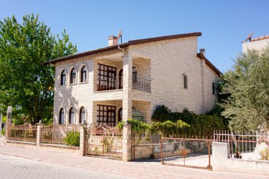 Güneşli bir günde, etrafı metal çitler ve açık mavi gökyüzüyle çevrili, kemerli pencereleri ve balkonu olan taş bir ev. Konut mimarisi kavramı
