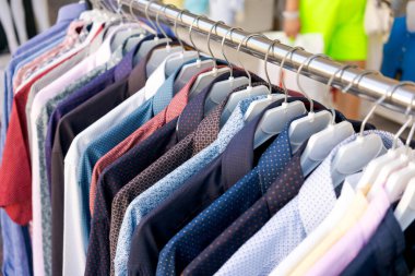 Mağaza vitrinindeki askılarda çeşitli renkte ve desenlerde çeşitli erkek gömlekleri. Arka plan bulanık, gömleklere odaklanmış. Moda perakende ve giyim anlayışı