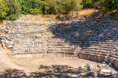 Etrafında taş bir duvar olan büyük taştan bir amfi tiyatro. Taş duvar büyük kayalardan yapılmıştır ve zemin toprakla kaplıdır. Amfi tiyatro boş ve güneş onun üzerinde parlıyor.