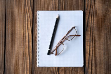 Bir kağıt parçasında bir kalem ve bir gözlük var. Kalem siyah, gözlük kahverengi.