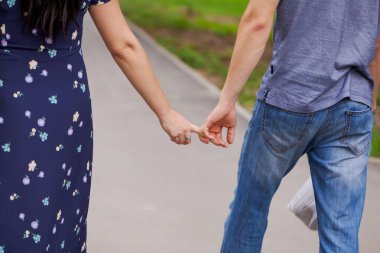 Kadın ve erkek kaldırımda yürürken el ele tutuşuyorlar. Kadın çiçekli bir elbise giyiyor ve erkek de mavi gömlek ve kot pantolon giyiyor. Sahne romantik ve samimi.