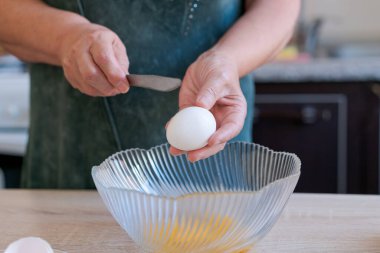 Kadın kaseye yumurta kırıyor. Yumurtayı kırmak için bıçak kullanıyor.