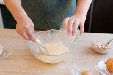 Kadın ahşap bir masada tatlı yapıyor. Malzemeleri karıştırmak için cam kase ve cam kavanoz kullanıyor.