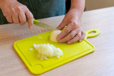 Yeşil kesme tahtasında soğan doğrayan biri var. Soğanlar küçük parçalara ayrılıyor.