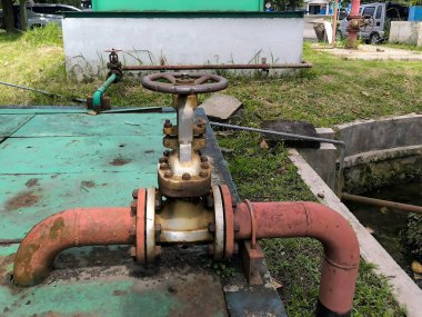 Paslı kırmızı boru hattında tekerlek sapı olan büyük bir sanayi kapısı vanası..