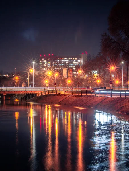 Geceleri bir nehir ve suda yansıyan ışıklar olan bir şehir.