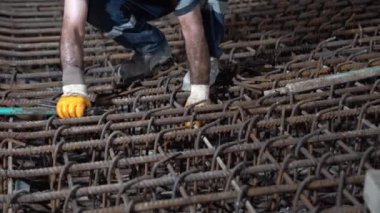 Bir işçi inşaattaki çelik destek çubuklarını eldiven takarak bağlıyor..