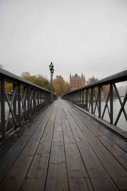 Stockholm 'de sonbaharda şehir manzarasının arka planında yaya ahşap köprüsü