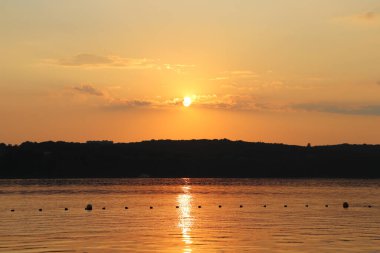 Gölün üzerinde günbatımının sihirli sahnesi, güneş suya yansıyor.