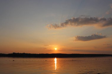 Gölün üzerinde günbatımının sihirli sahnesi, güneş suya yansıyor.
