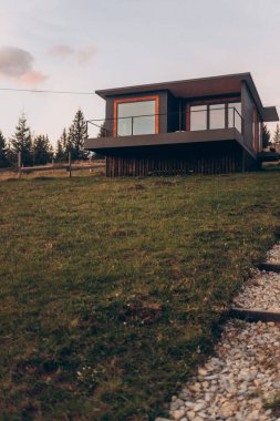 Geniş bir bahçesi ve yolu olan bir ev. Ev ağaçlarla çevrili ve büyük bir penceresi var.