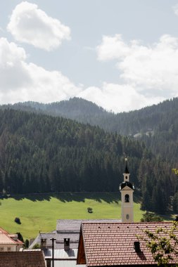 Uzakta bir kilise olan bir dağ sırası. Gökyüzü bulutlu ve güneş parlıyor