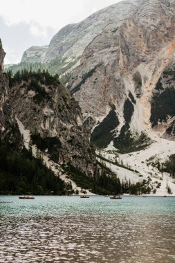 Önünde Lago di Braies gölü olan bir dağ sırası. Göl tekneler ve insanlarla dolu.