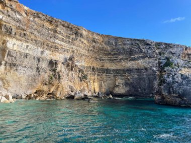 Comino adasında nefes kesici kıyı güzelliği: mavi gökyüzü, görkemli uçurum, sakin deniz.
