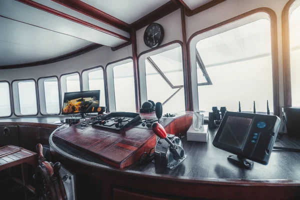 A wide-angle perspective view of a vessel dashboard with plenty of instruments, dial indicators, and other navigational equipment; a yacht control panel on the captain\'s bridge with a compass