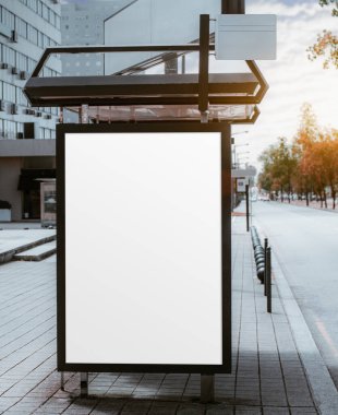 Ticari kullanım için bir otobüs terminalinde boş bir dikey reklam modeli, konut binasının yanında ve öğleden sonra güneşinin parlaması bulutlar tarafından gizlenmiş; otobüs durağındaki boş reklam tutucu şablonu