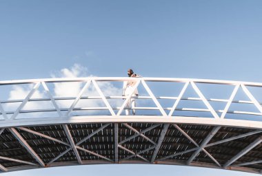 Beyaz takım elbiseli, bakımlı sakallı, züppe, kel, Afro-Amerikan bir yöneticinin parlak bir günde beyaz metal bir köprüde eskrim yaparken çekilmiş düşük açılı bir fotoğrafı.
