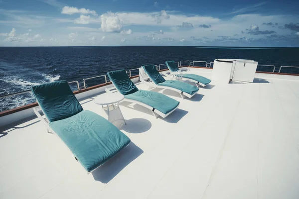 A shot of a four lounge chairs in a row with blue cushions lining them on the upper deck of a luxury diving safari yacht sailing around the Maldives island on a shiny day with some clouds in the day