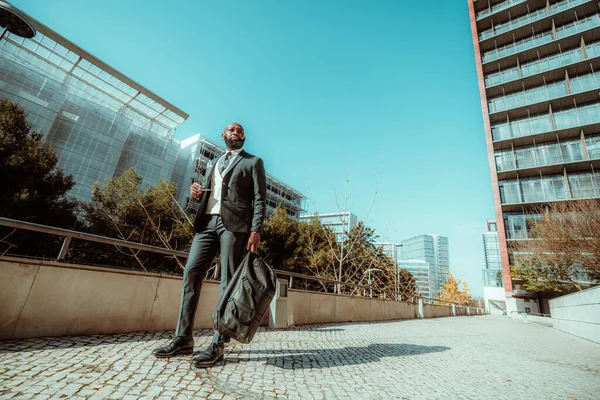 一位优雅的安哥拉男子站在办公大楼外的葡萄牙鹅卵石人行道上 身穿格子西服 在阳光明媚 蔚蓝的天空中扛着一个周末的记事本 — 图库照片