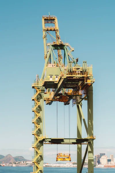 Vertical zoomed-in view of a heavy yellow industrial crane machinery with the blue cloudless sky in the background, with a big cabin, many stairways, cables, and passages with fences on its top