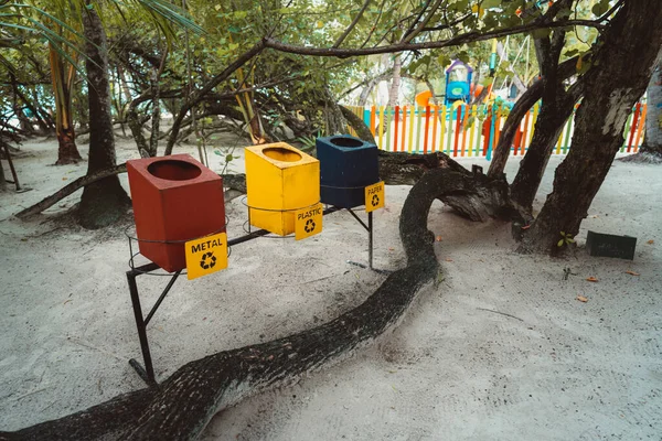 在白色沙滩上 三个收集垃圾的木制回收容器被抬高到人类的高度 红色代表金属 黄色代表塑料 蓝色代表纸张 还有一个树干 右边是树干 — 图库照片