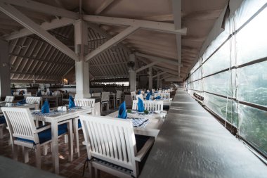 Restoranın köşesinde, gözlerimiz ahşaptan yapılmış el değmemiş beyaz masalara ve sandalyelere çekiliyor, peçetelerin ve sandalye minderlerinin koyu mavi aksanlarına karşı yatıştırıcı bir kontrast oluşturuyor.