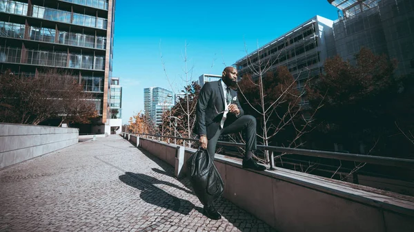 エレガントな黒の男は 屋外でリラックスして バックグラウンドでは 完全なスーツを着てポルトガルの石畳の歩道に立って 晴れと青い空の日に週末を運ぶ — ストック写真