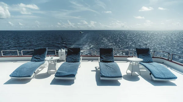 在马尔代夫的场景中 有一艘豪华游艇在平静的水面上 甲板上有蓝色靠垫的躺椅 灿烂的阳光加强了蓝天和大海的力量 营造出宁静而迷人的氛围 — 图库照片