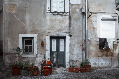 Tahta kapılı, eski pencereli ve kaldırımın önündeki kaldırım taşının üzerinde bitki bulunan bir grup çiçek saksısı olan, yıpranmış eski bir Avrupa evinin ön cephesinin ön görüntüsü.