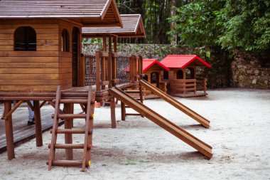 Çocuk ahşap oyun evi ve kumlu bir oyun parkında kayar. Aktif bir oyunu doğal ortama davet eder.