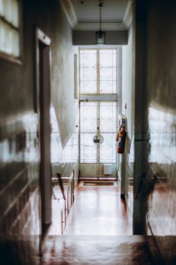 Seçici odak noktası, arka planda cam camlı bir kapı, kartonpiyer duvarlar, yangın söndürücü ve asılı bir lamba armatürünün bulunduğu vintage bir koridor.