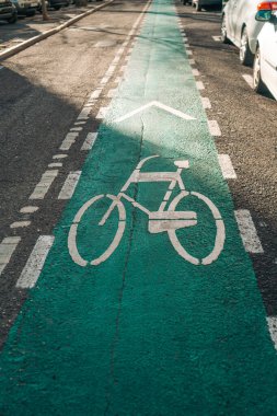 Şehir caddesindeki bisiklet yolunun beyaz bisiklet sembolü ve yeşil boyayla işaretlenmiş yakın görüntüsü. Güneş asfalta gölge düşürür. Bisiklet altyapısı temaları için ideal