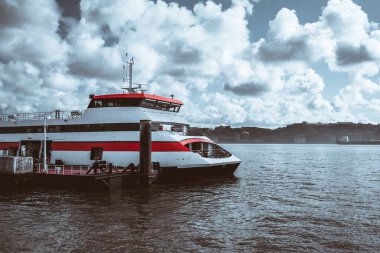 Modern bir yolcu feribotu bulutlu bir günde rıhtıma yanaştı. Feribot kırmızı ve beyaz renkli bir şemaya sahiptir ve arka planda su ve uzak tepeler olan ahşap bir rıhtıma demirlemiştir; Lizbon, Portekiz