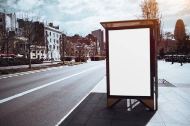 Boş otobüs durağı olan bir şehir caddesi sahnesinde büyük boş bir reklam panosu var. Çevrede binalar, ağaçlar ve açık bir gökyüzü vardır. Pazarlama ya da reklam modeli için ideal.