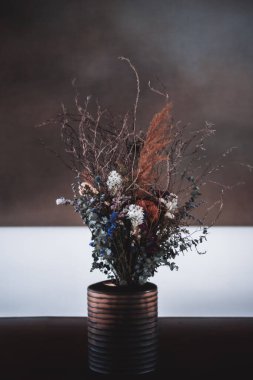 Kurumuş çiçek ve dalların seramik bir vazoda bir karışımının yer aldığı bir çiçeğin dikey detaylı fotoğrafı. Sığ alan derinliği