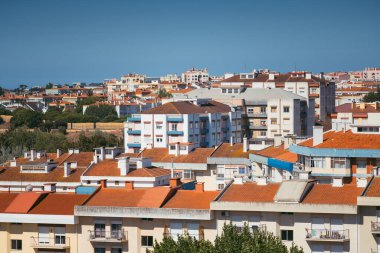 Lizbon 'un konut alanının panoramik manzarası. Kırmızı kiremitli çatıları ve çeşitli mimari tarzları olan çok sayıda bina var. Açık mavi gökyüzü canlı şehir manzarasını güçlendirir