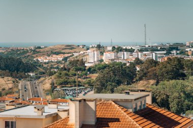 Lizbon banliyö bölgesinin panoramik manzarası. Konut binaları, ağaçlar ve ufka doğru giden yollar. Modern apartmanlar, yemyeşil manzaralar, yukarıda açık mavi bir gökyüzü.