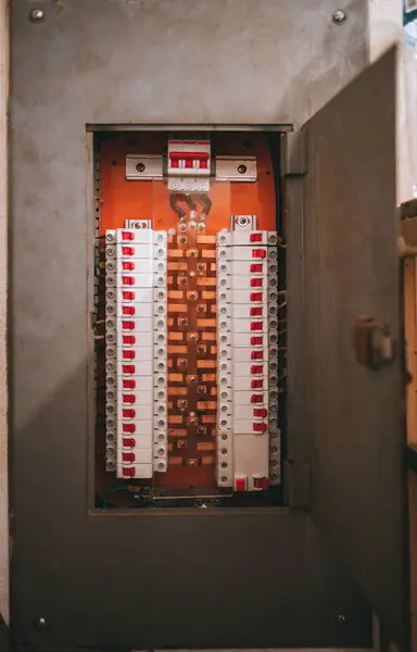 stock image An open electrical panel with numerous circuit breakers and a neatly organized wiring system. The breakers have red switches and are arranged symmetrically on a metallic backing, in the panel box