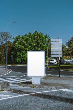 Vertical shot of Mockup of a blank billboard and empty direction signposts at a city roundabout. Clear sky, greenery, and street visible. Perfect for outdoor advertising and sign mockup presentations clipart